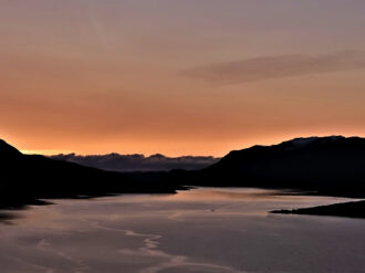 Spectacular orange sky after sun dips below the mountainsides of the fjord.