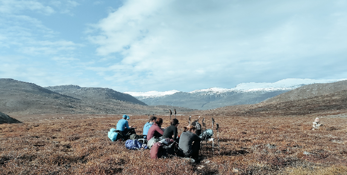 The team of trekkers sit on their heavy packs in the last of the day's heat and snack